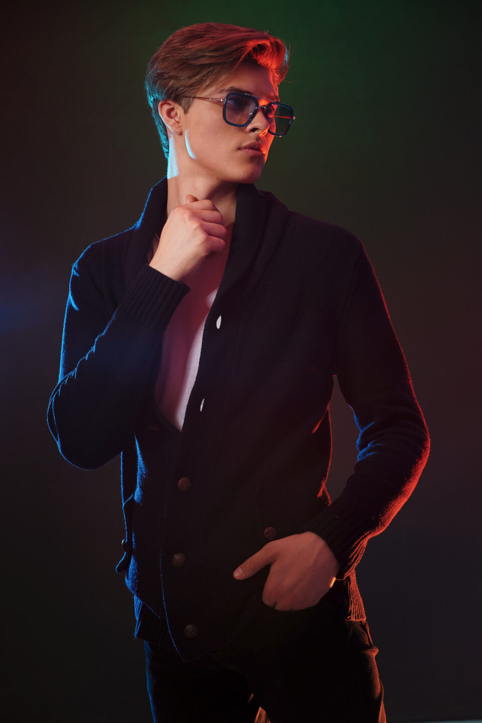 Trendy young man with cool hairstyle wearing black jacket with sunglasses. High Fashion male model posing on black background. Art design concept